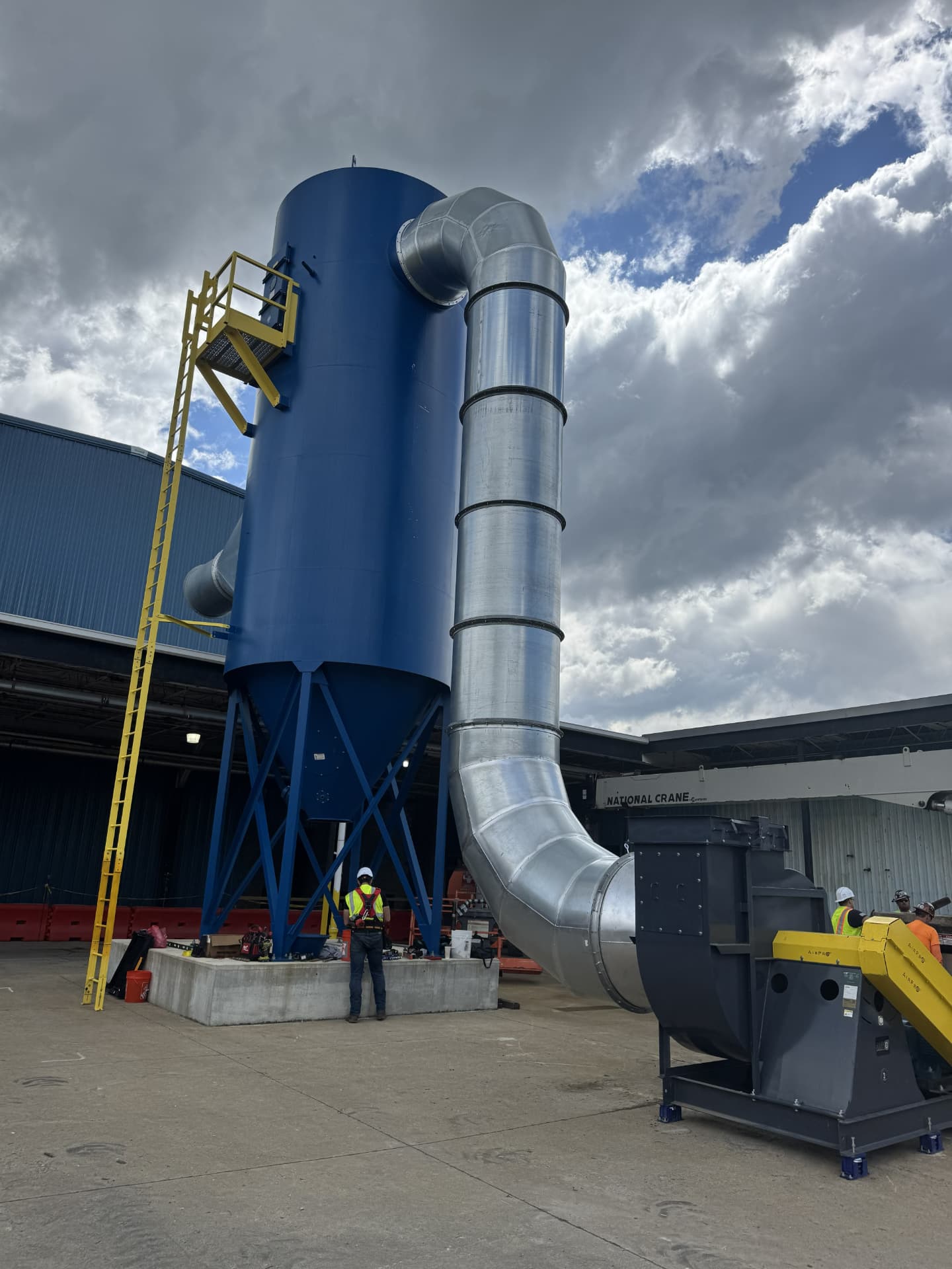 JD Indoor Comfort technician beside a large blue industrial dust collector and spiral duct system at a Northeast Ohio manufacturing plant