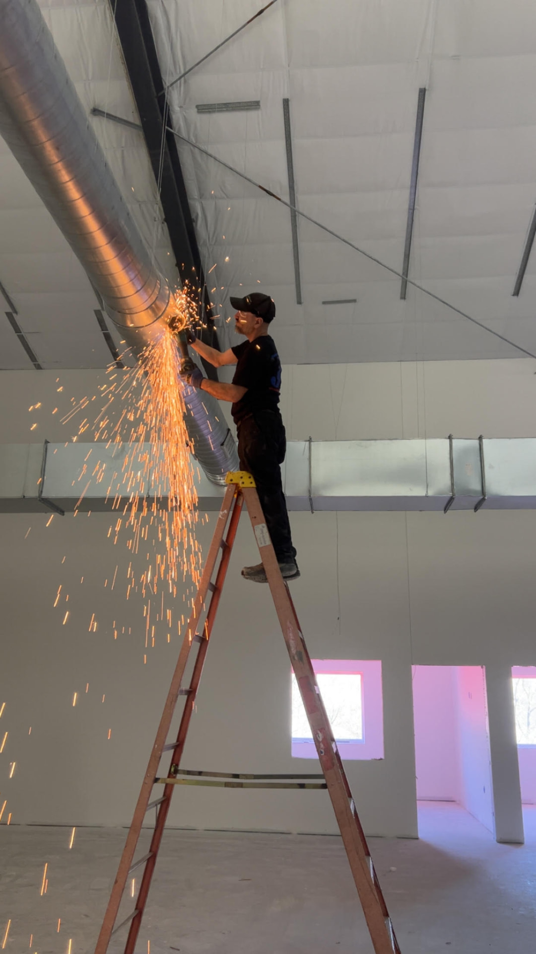 JD Indoor Comfort sheet metal technician cutting spiral ductwork on a commercial build-out, sparks flying