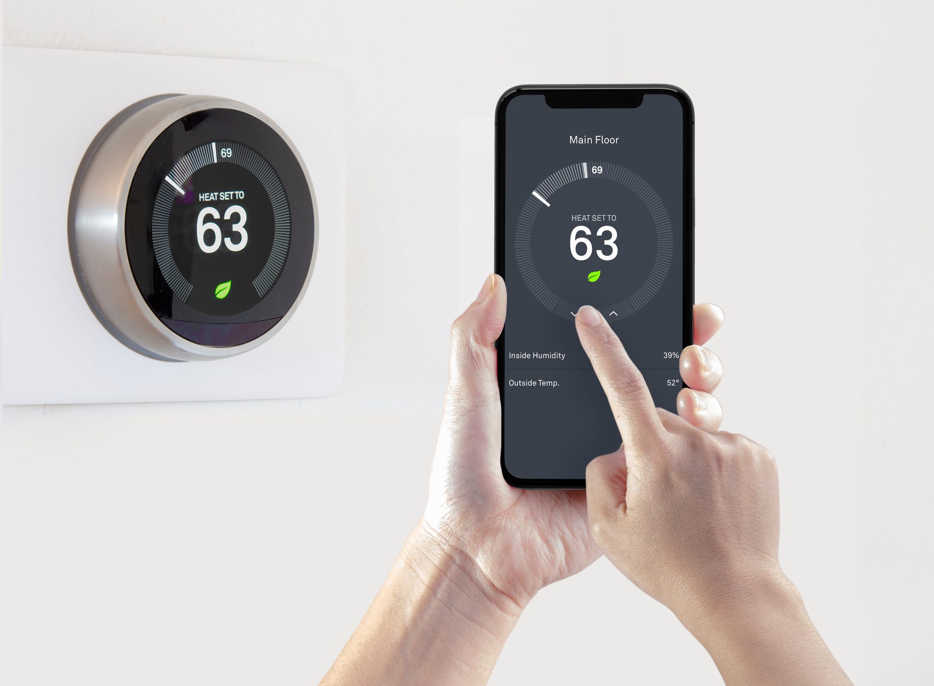 Homeowner adjusting a smart thermostat from a phone app beside the wall-mounted thermostat