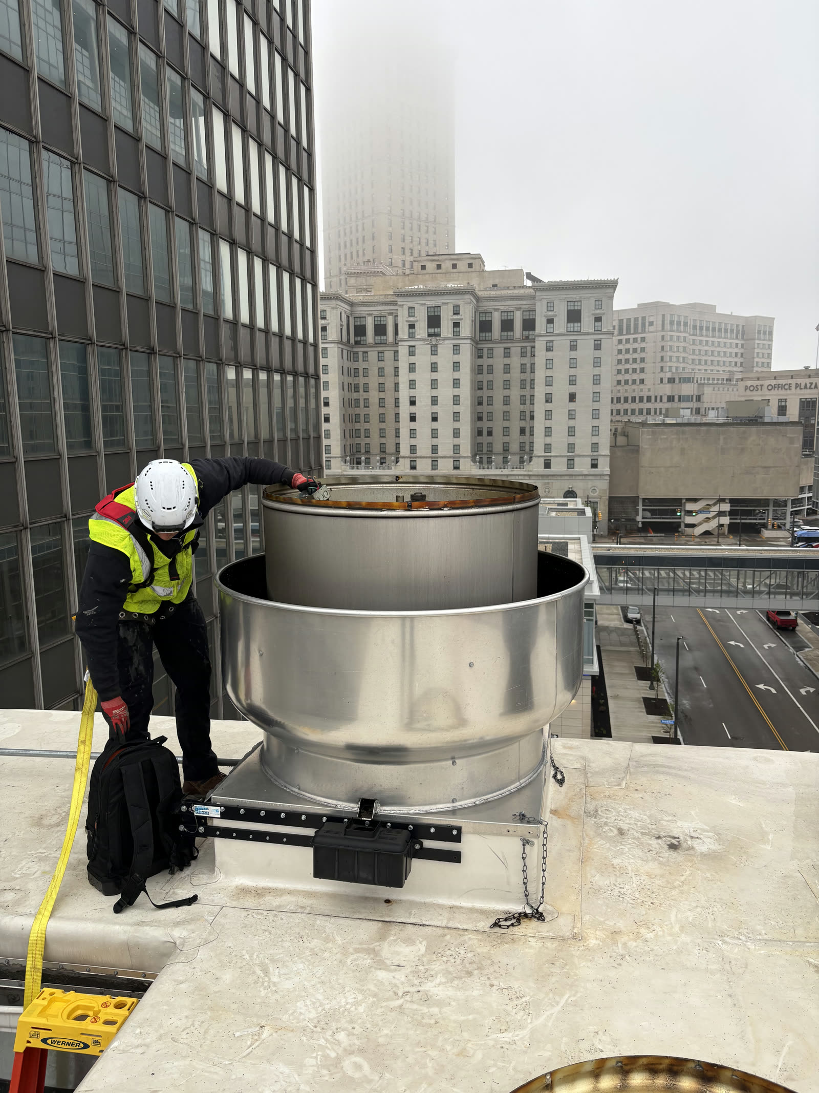 JD Indoor Comfort technician rigging a stainless steel commercial exhaust fan on a Cleveland rooftop overlooking Public Square